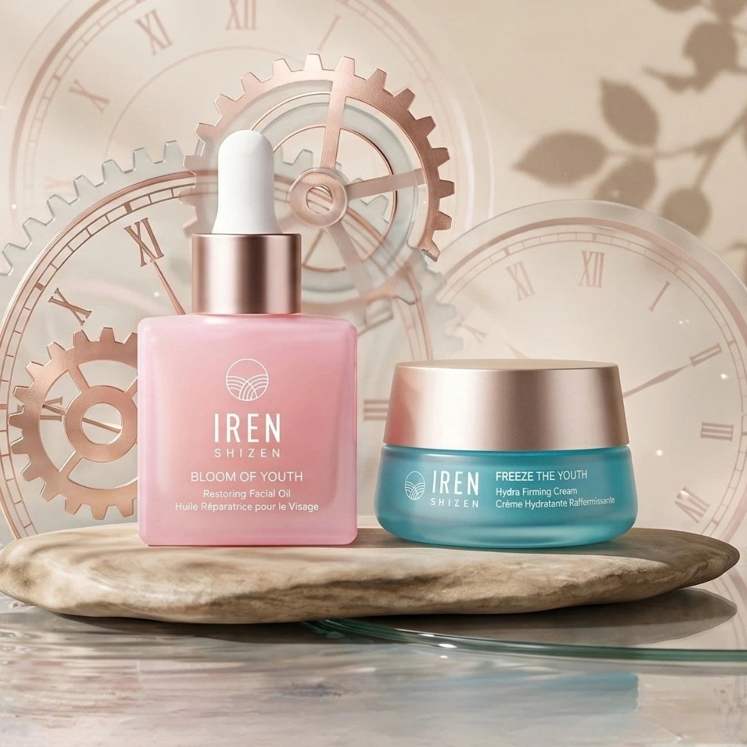 A pink glass bottle of collagen-boosting facial oil and a teal jar of firming cream from the TIME REBOUND Lift and Firm Kit sitting on a stone slab against a clock-themed background.