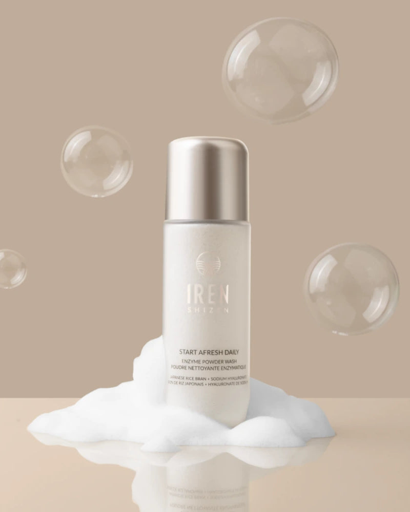A bottle labeled "IREN Shizen" stands on a mound of foam with floating bubbles against a beige background, presenting the START AFRESH DAILY Enzyme Powder Wash, a gentle daily exfoliant rice enzyme cleanser.