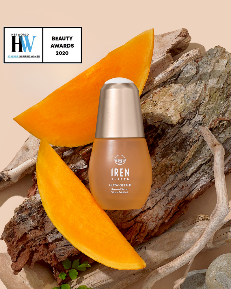 A bottle of IREN Shizen GLOW-GETTER Renewal Serum sits on wood with pumpkin slices. Formulated with Pumpkin Seed Extract for gentle exfoliation. A "Beauty Awards 2020" badge is shown in the top left corner.