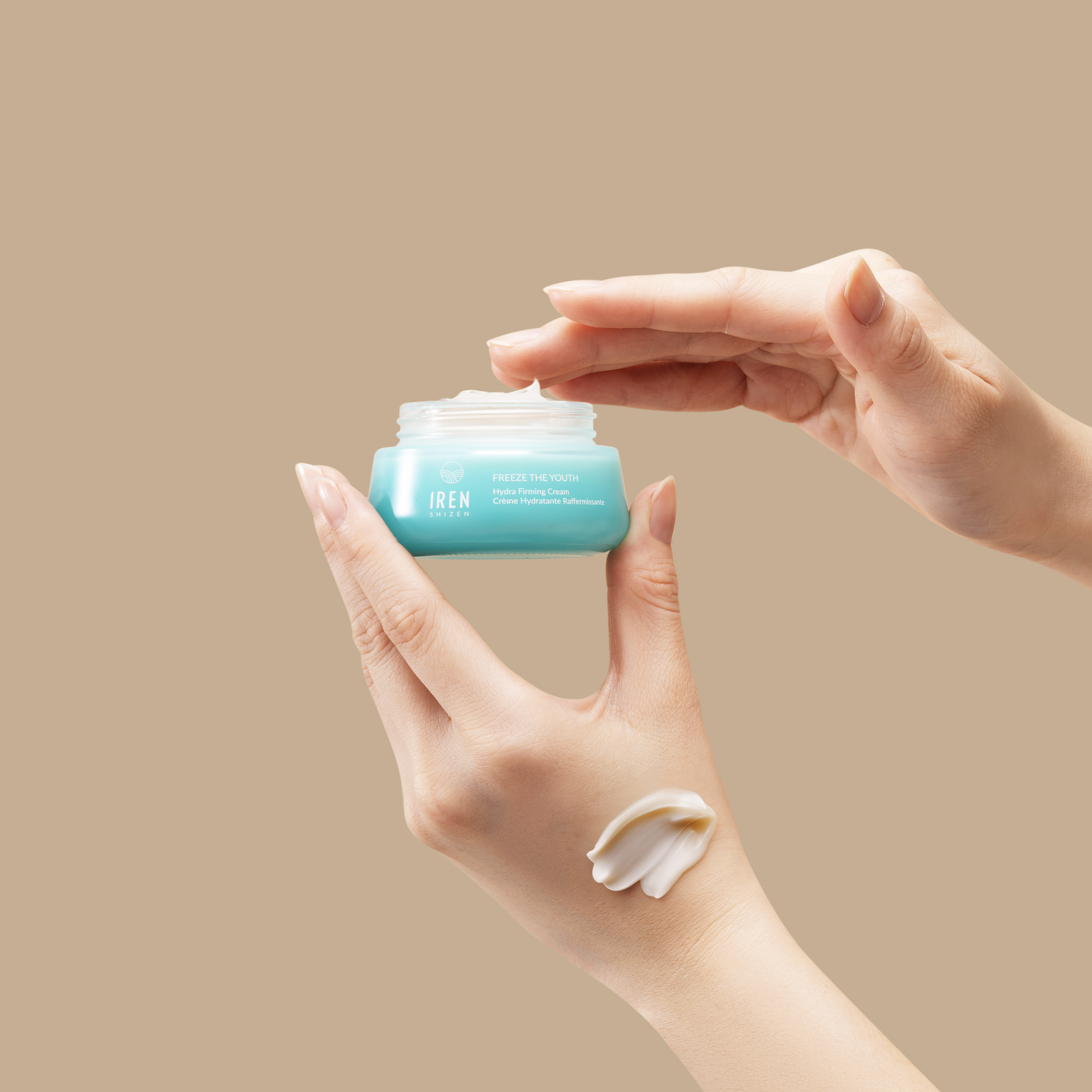 A hand holds a blue jar from the IREN Shizen MOISTURE SANDWICH Skincare Kit while another dips in; cream is swatched on the lower hand, showcasing hydration and a strengthened moisture barrier against a beige background.