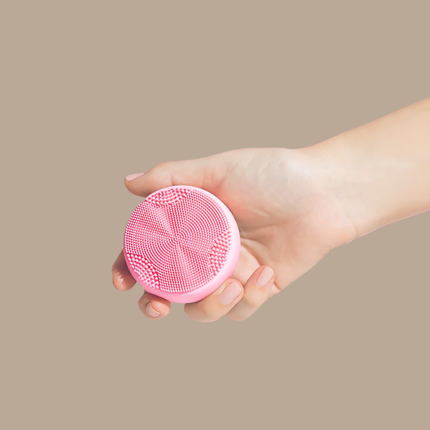 A hand holds the pink, round GLOW ON THE GO Travel Light Kit by IREN Shizen against a plain beige background—an essential for any travel skincare routine.