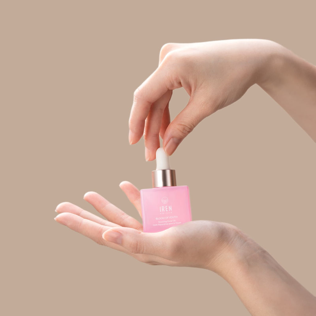 A youthful woman's hand holding a BLOOM OF YOUTH Restoring Facial Oil bottle by IREN Shizen.