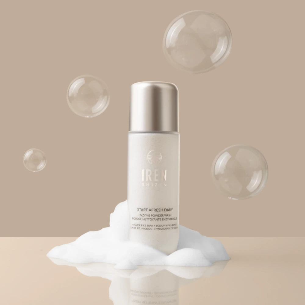 A bottle labeled "IREN Shizen" stands on a mound of foam with floating bubbles against a beige background, presenting the START AFRESH DAILY Enzyme Powder Wash, a gentle daily exfoliant rice enzyme cleanser.