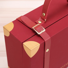 The FOR BELOVED ONES Xmas Luggage Gift Box by IREN Shizen features a red suitcase adorned with gold corner protectors and a leather strap with a buckle.