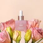 A pink dropper bottle labeled "BLOOM OF YOUTH Restoring Facial Oil" by IREN Shizen sits among pink and yellow flowers against a light beige background, highlighting its lightweight formula that supports skin barrier repair. #all-groups