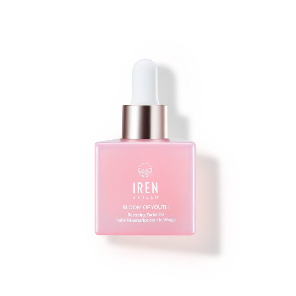 A pink lightweight BLOOM OF YOUTH Restoring Facial Oil bottle with a dropper, floating against a matching swatch-background by IREN Shizen.