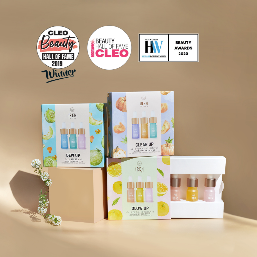 Four IREN Shizen CLEAR UP Anti-Blemish Discovery Kits and three individual serum bottles are displayed on a light brown surface with shadows, featuring award badges in the background.