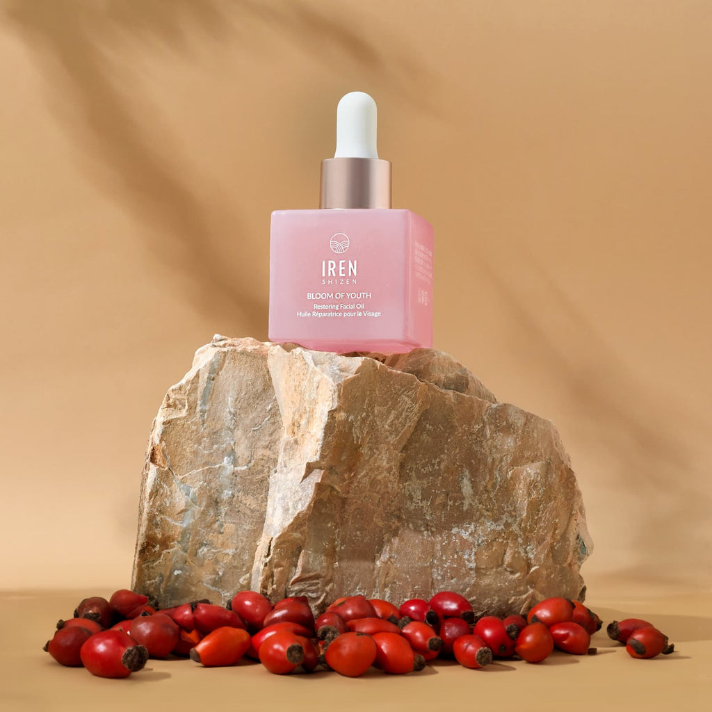 A firm bottle of BLOOM OF YOUTH Restoring Facial Oil by IREN Shizen sitting on top of a rock, promoting youth and prebiotics.