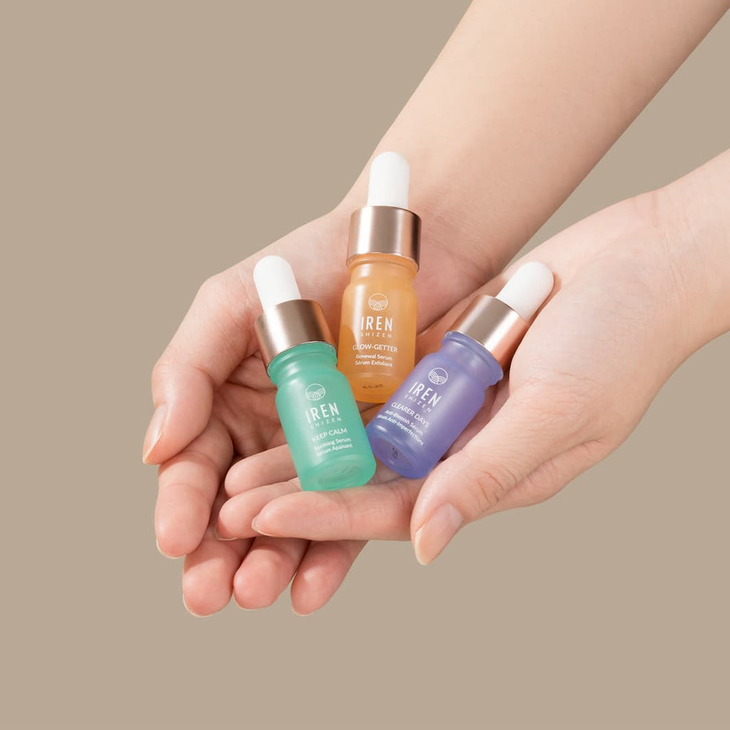 A woman's hands holding three different types of IREN Shizen's CLEAR UP Anti-Blemish Discovery Kit serums.