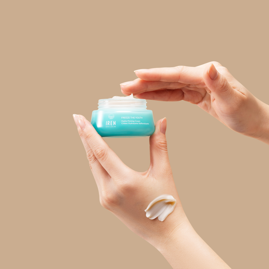 A person holding a jar of FREEZE THE YOUTH Hydra Firming Cream from IREN Shizen.
